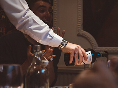 A waiter pouring wine infront of a delighted customer